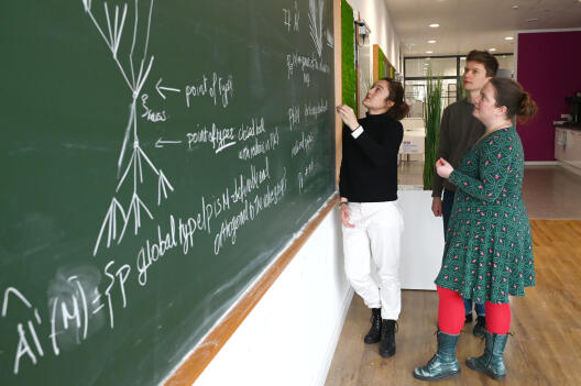 Mariana Vicaria, Floris Vermeulen and Franziska Jahnke discussing at the blackboard.