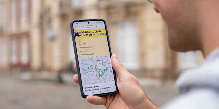 Ein junger Mann hält ein Smartphone in der Hand. Auf dem Smartphone ist ein Lageplan des Hochschultags zu sehen.<address>© Uni MS - Johannes Wulf</address>