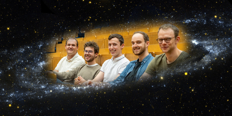 Das Bild ist eine Montage aus zwei Fotos. Es zeigt die Physikdoktoranden Philipp Schulte, Johannes Pirsch, Richard Salomon, Richard von Eckardstein und Justus Kuhlmann (v. l.) vom Astroseminar-Team 2024 sitzend in einem Hörsaal. Sie sind scheinbar umgeben von einer Galaxie.<address>© Montage: Uni MS - Johannes Wulf/ NASA/JPL/California Institute of Technology</address>