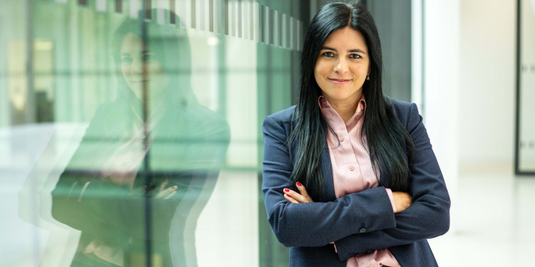 Dr Maria Florencia Sánchez stands with folded arms in front of a glass pane in which her reflection can be seen.<address>© Uni MS - Johannes Wulf</address>