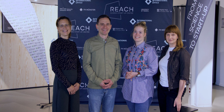 Vier Personen stehen vor einem Banner mit dem Logo des REACH – EUREGIO Start-up Center. Maria Homeyer, Dr. Christian Wiencierz, Dr. Natalie Powroznik und Katy Krukar (v.l.).<address>© Uni MS</address>