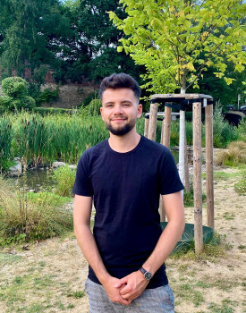 Doctoral student Marc Bauhus is standing in a dark blue T-shirt in front of a small tree with green leaves in a meadow.<address>© Uni MS - IEB</address>