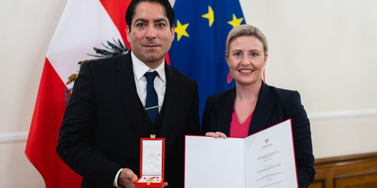 Zu sehen sind Prof. Dr. Mouhanad Khorchide, der eine Schatulle mit dem Goldenen Ehrenzeichen in der rechten Hand hält, und die Bundesministerin Susanne Raab mit einer Urkunde für ihn.<address>© BKA/Florian Schrötter</address>