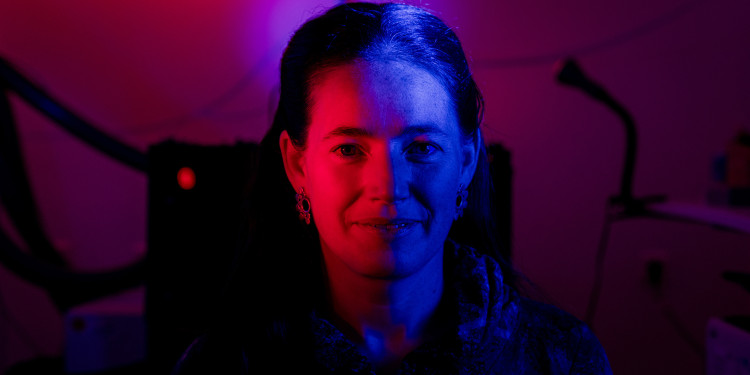 A portrait of Prof Seraphine Wegner. Her face is illuminated in red from the left and in blue from the right. In the background, laboratory equipment can be seen out of focus.<address>© Uni MS - Florian Kochinke</address>