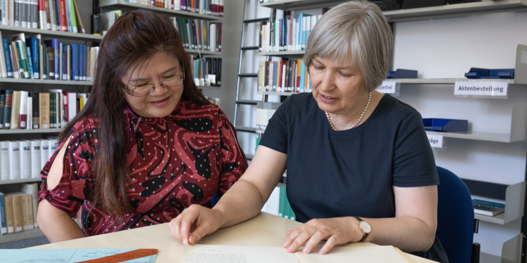 Gemeinsam mit Dr. Sabine Happ (r.) blättert Dong-Nan Zhu durch die Bescheinigungen und Urkunden ihrer Großmutter.<address>© Uni MS - Linus Peikenkamp</address>