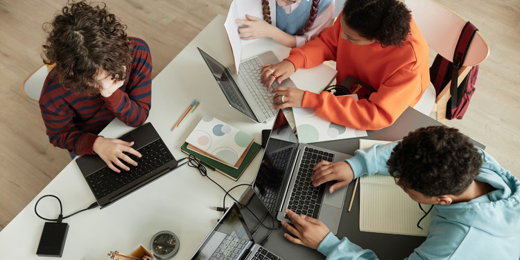 Jugendliche sitzen um einen Tisch herum und arbeiten an Laptops; von oben fotografiert<address>© stock.adobe.com - Seventyfour</address>