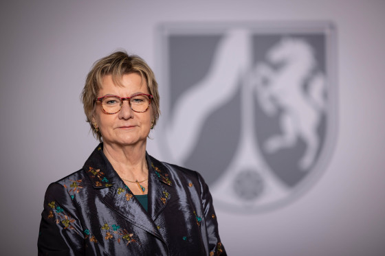 Zu sehen ist ein Porträtfoto von Sylvia Löhrmann, im Hintergrund ist das nordrhein-westfälische Landeswappen zu sehen.<address>© Staatskanzlei NRW</address>