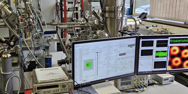 Ein Blick ins Labor. Im Hintergrund ein Rastertunnelmikroskop, im Vordergrund zwei Monitore mit mikroskopischen Aufnahmen und Daten.<address>© Uni MS - Harry Mönig</address>